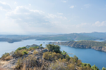 Panoramic view of a turquoise reservoir surrounded by green mountains under a cloudless, intense blue sky in midsummer