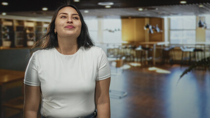 Woman with bare arms smiling and mouth slightly open while looking upward in hotel lobby, casual...
