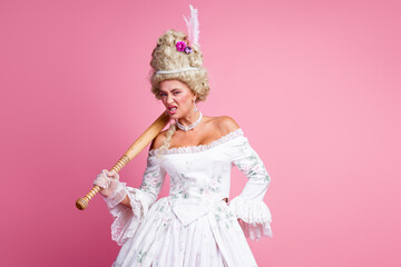 Elegant young aristocratic woman in historic baroque costume on pink background showcasing bold expression with bat