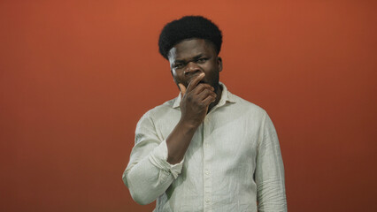 Man african american wearing light linen shirt holding hand to forehead in studio on orange wall, signaling headache and visible discomfort; pain fatigue.