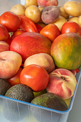Colorful arrangement in a refrigerator drawer where scarlet tomatoes, yellow potatoes, deep red bell peppers, and orange nectarines create a rainbow of colors