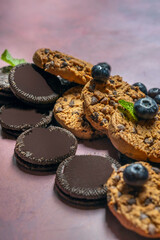 Casual cafe scene with a tray containing several cookies, a blueberry smoothie with whipped cream, and fresh blueberries on a table with a lilac background