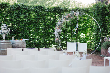 Hochzeitszeremonie im Freien mit Blumenkreis und weißen Stühlen