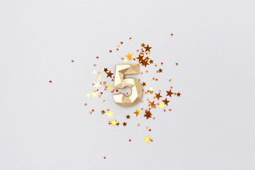 Golden number 5 and stars confetti on a blue background. Festive composition.