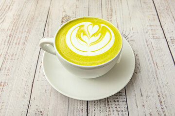 A clear cup with a modern, frothy matcha latte, viewed from above against a light brown background, highlighting its texture and green hue