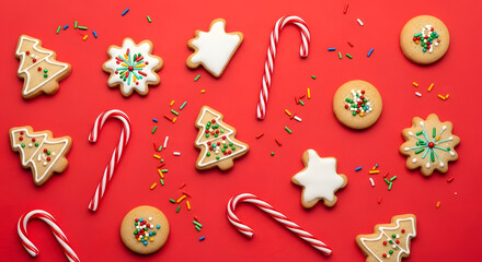Christmas cookies and candy canes arranged on a red background with colorful sprinkles scattered around