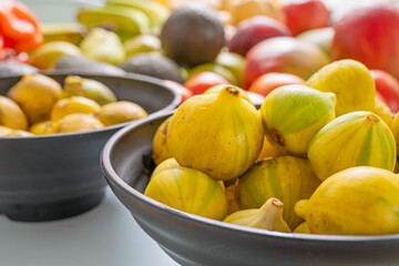 Artistic arrangement of natural foods: black figs, yellow pears, green avocados, new potatoes, and red nectarines on a pastel blue surface