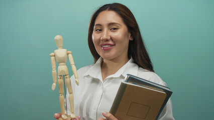 Woman holding wooden mannequin and notebooks in mint green studio; creativity education confidence.