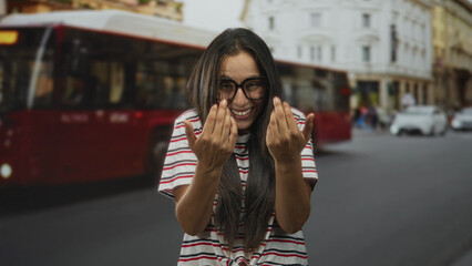 Fototapeta premium Woman with glasses and striped shirt beckons with hands on a busy city street beside a red bus and classical building; playful.