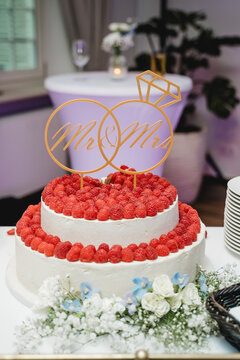 Hochzeitstorte mit frischen Himbeeren und Blumen, elegante zweist&ouml;ckige Festtagstorte auf Bankett-Tisch