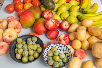 Contemporary still life with yellow bananas, green pears, ripe avocados, earthy potatoes, orange nectarines, and purple figs on a pastel blue table