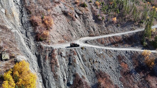 Aerial view of a rugged, winding dirt road clinging to the steep mountainside as a lone vehicle navigates the challenging terrain, Telluride, Colorado, United States.