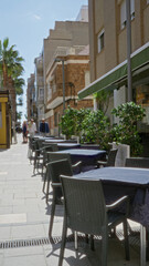 Street cafe scene in torrevieja with empty tables and chairs under the sunny sky, surrounded by palm trees and residential buildings, capturing the peaceful spanish outdoor ambiance.