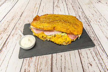 Giant Venezuelan patacones topped with stewed shredded chicken, sliced ​​avocado, and refried black beans with bacon