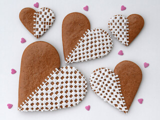 Decorated heart-shaped gingerbread cookies in three sizes with small sugar hearts on a white...