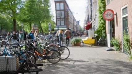 Naklejka premium Blurred scene in amsterdam with bicycles parked on the street and people in the distance, creating a vibrant, out-of-focus urban atmosphere with lush greenery and buildings.