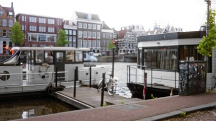 Blurred scene of floating house and boat on amsterdam canal with defocused architecture and street.
