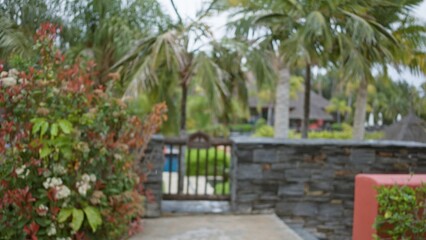 Blurred view of a tropical resort with lush greenery and palm trees, capturing a serene, luxurious outdoor setting with stone walls and vibrant flowers in the background.