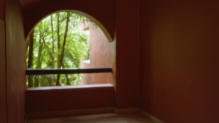 Defocused view of tropical greenery through an arched window in a luxury resort, creating a serene and inviting atmosphere with a blurred, calming ambiance perfect for relaxation.
