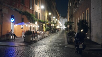 Night cobblestone street with cafe terraces and parked scooter, defocused bokeh street; background backdrop copyspace.