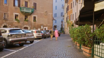 Cobblestone street scene blurred into warm soft bokeh with parked cars, planters and historic facades in shallow focus street; background backplate copyspace template.