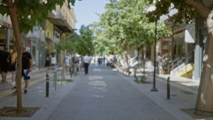 Fototapeta premium Blurred urban scene with trees, storefronts and tiled sidewalk, soft shallow bokeh and defocused foreground street; background backplate copyspace calm.