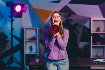 Young female blogger broadcasting with a megaphone in a vibrant neon lit studio showcasing creativity and confidence