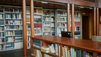 Blurred library stacks and wooden reference desk in shallow focus interior with bookshelves and pillars; background backplate copyspace template.