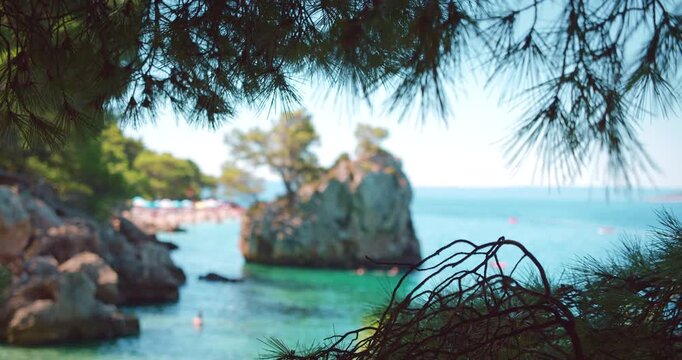 Popular beach in Croatia with large rock in sea and tourists swimming on sunny day