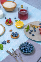 An overhead view of a table with a light blue tablecloth displaying a blueberry cheesecake, alongside two refreshing drinks