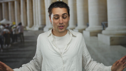 Obraz premium Young hispanic man in casual attire gesturing outdoors with columns in the background of an old town setting in ambient daylight