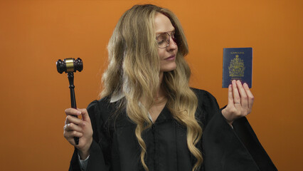 Woman judge in black robe holding canada passport and gavel against orange background, symbolizing law and immigration authority.