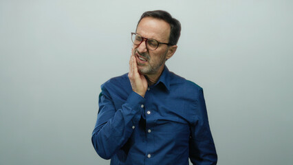 Hispanic man experiencing tooth pain against a white background, clutching his jaw with a pained...