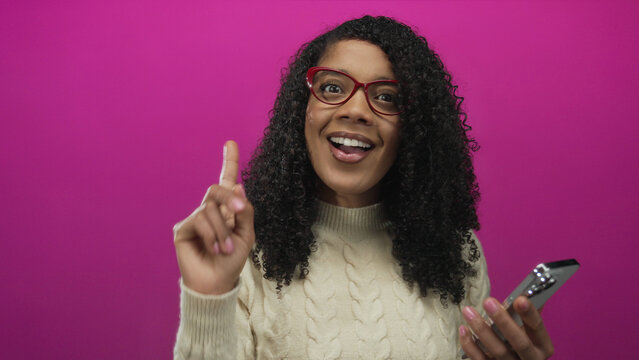 Woman scratches head holding smartphone in studio setting with bright pink backdrop while frowning at the screen; confusion.