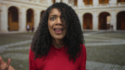 African american woman touching her curly hair and gesturing with open palms in a historic building...