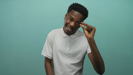 Young african american man smiles and pinches fingers to show a tiny gap in teal studio;...