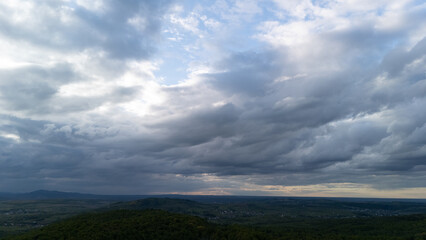 Aerial landscape of cloudy mountain horizon and vast green forests with patches of sunlight, illustrating calm power of nature and stunning wilderness perspective