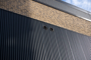 Industrial building facade with corrugated metal cladding and brick detail, combination of textures and materials. For architecture, industrial design, construction, facade materials. Real photo