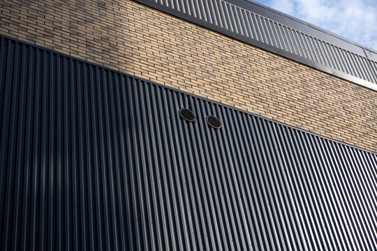 Industrial building facade with corrugated metal cladding and brick detail, combination of textures and materials. For architecture, industrial design, construction, facade materials. Real photo