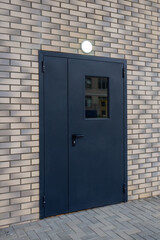 Black metal door with small window in light brick wall. Exterior entrance for commercial, industrial or institutional building. Real photo