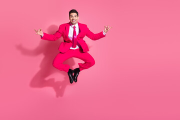 Expressive young man in vibrant pink suit enjoying a joyful jump against a matching background exuding stylish fun
