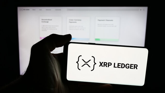 Stuttgart, Germany - 10-17-2025: Person holding mobile phone with logo of cryptocurrency platform XRP Ledger (XRPL) on screen in front of web page. Focus on phone display.