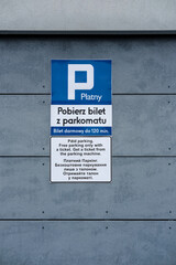 Paid parking sign in Polish, English, and Ukrainian languages mounted on a gray concrete wall.