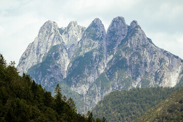 Aerial view of the stark, jagged peaks rise majestically against the softer green foothills, a symphony of stone and verdant life, Tarvisio, Friuli-Venezia Giulia, Italy.