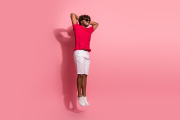Young man in casual red T-shirt and white shorts jumping joyfully against a pink background, enjoying leisure time