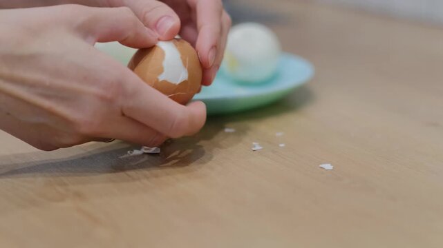 Hands of woman peeling boiled chicken egg, showcasing care in food preparation. Soft texture revealed, perfect for salads, sandwiches, or snacks, emphasizing simplicity of cooking.