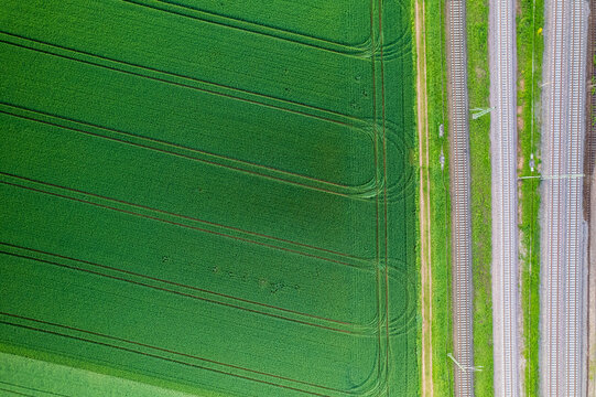 Aerial view of parallel lines of vibrant green fields and grey railway tracks create a striking contrast, Mannheim, Baden-Wurttemberg, Germany.