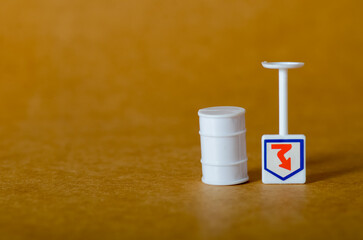 A miniature white oil barrel and a warning sign with a downward arrow symbolize falling prices and a negative market trend in the petroleum industry.