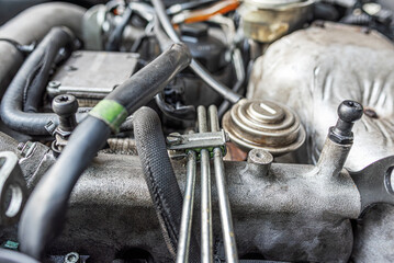 A car engine compartment showing detailed mechanical components, cables, and hoses in an automotive maintenance or engineering setting.
