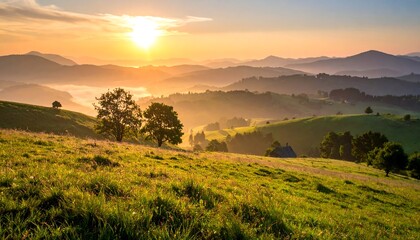 Fototapeta premium Golden sun rises over green hills with distant mountains and light fog, creating a serene landscape vista